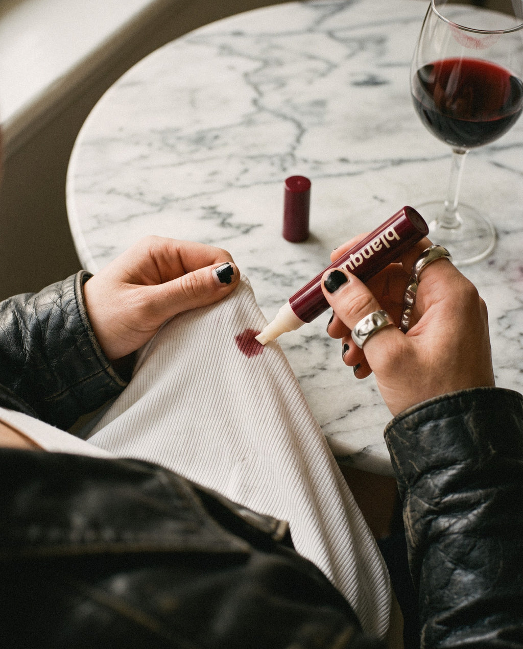 Pressing the chisel tip of a blanque pen onto a red-wine drop on a white ribbed top