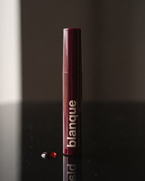 The glossy bordeaux pen standing on black glass with its reflection and one drop of red wine.