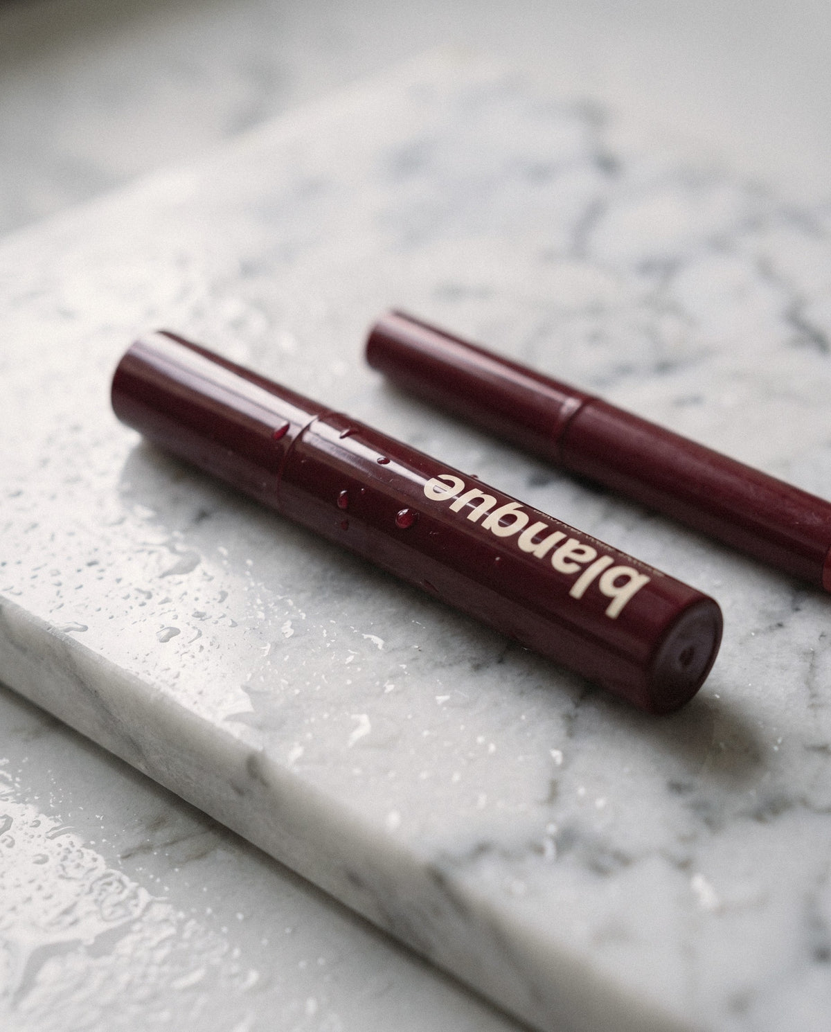 The pen on wet white marble next to a lipstick for scale.