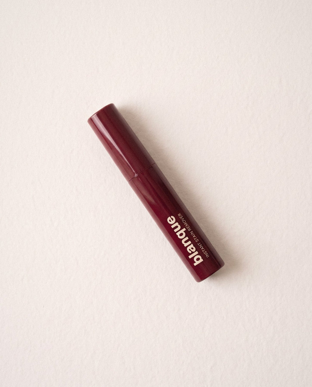 The glossy bordeaux pen lying on off-white paper, window light from the left.