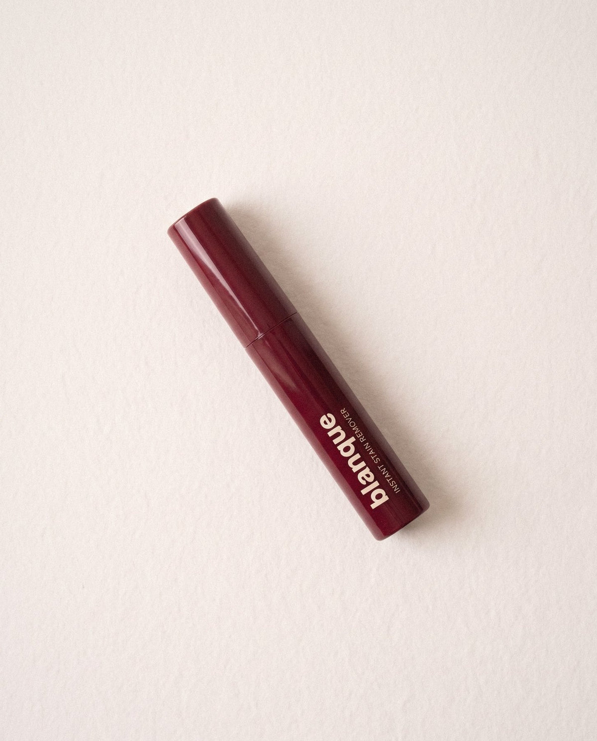The glossy bordeaux pen lying on off-white paper, window light from the left.